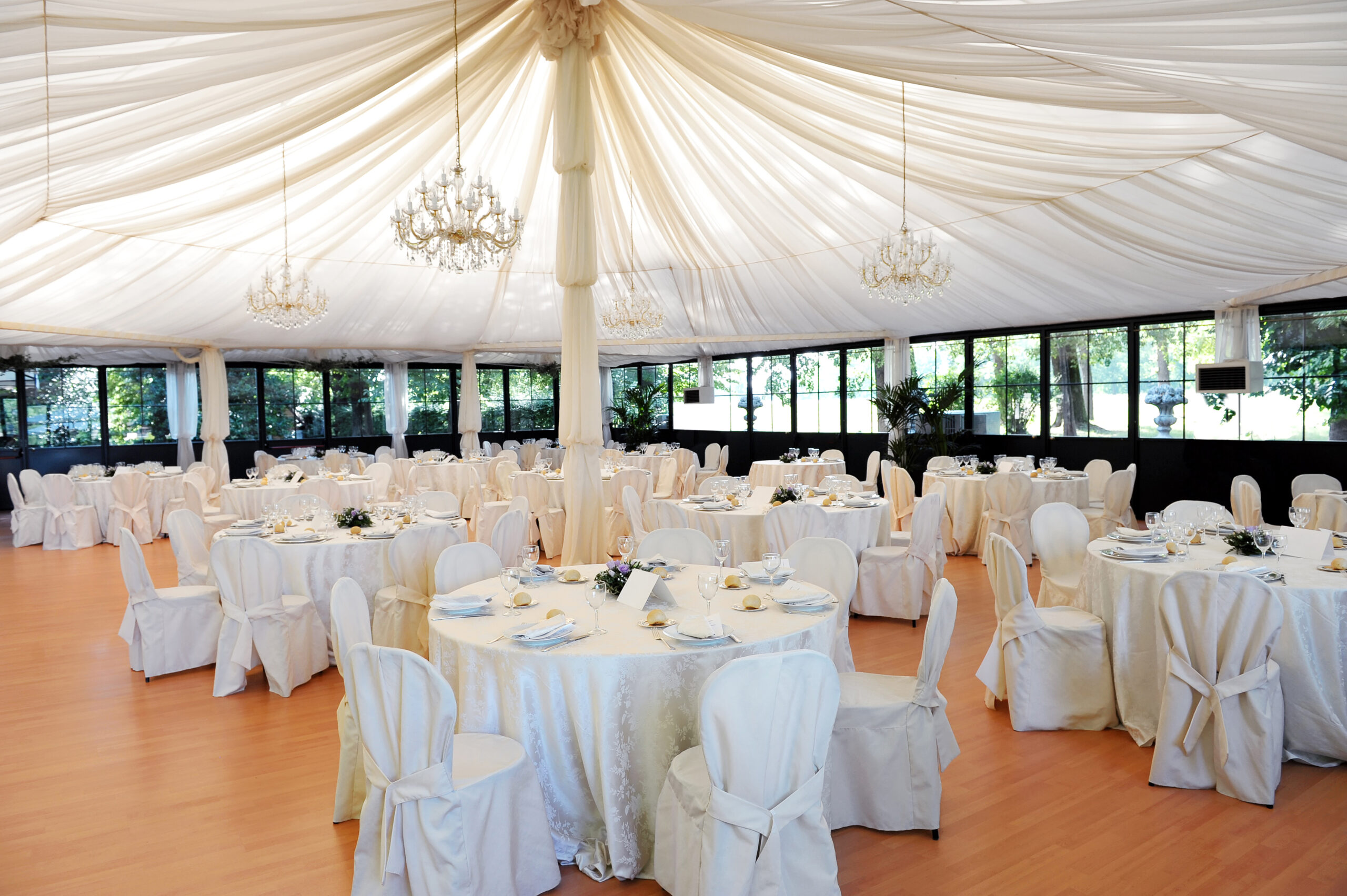 Wedding venue under a marquee with decorated tables and chairs draped in white linen around a central pole supporting the canvas